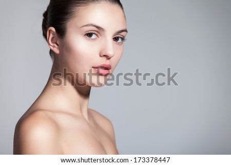 Closeup of a naturally beautiful woman with flawless skin gazing at you on gray