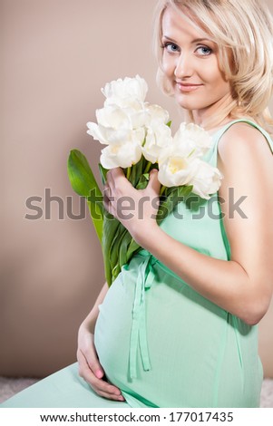 Pregnant woman wearing long green dress, holding in hands bouquet of  flowers, new life concept