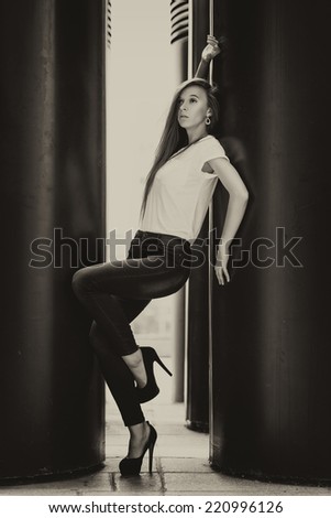 Full length portrait of a fashion model posing near large black pillars. Black and white photo.