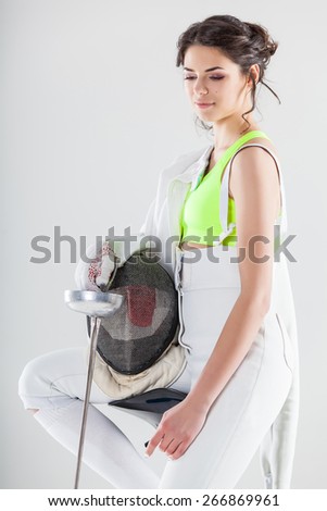 Smiling girl wearing white fencing costume holding the fencing mask and a rapier