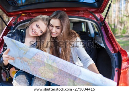 Two young women sitting in a trunk of car look at road map