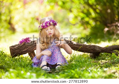 Summer portrait of cute blond girl dressed wreath of lilac on a head in green field.