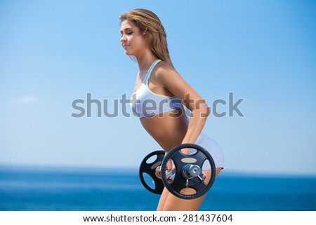 Shot of attractive young woman doing squats with a barbell outside
