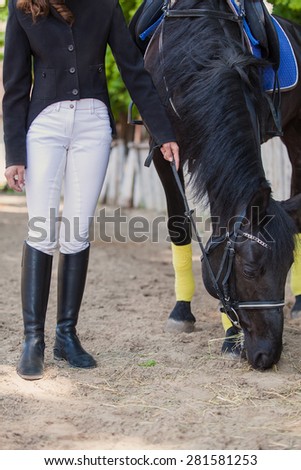 horsewoman jockey in uniform standing with black horse outdoors