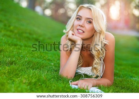 Happy young Caucasian blonde woman with tablet in park on sunny day on grass. Modern lifestyle and relaxation concepts.