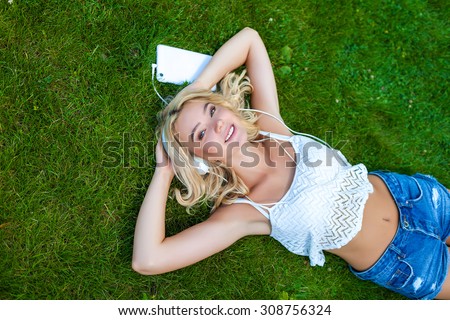 Happy young Caucasian blonde woman with tablet in park on sunny day on grass. Modern lifestyle and relaxation concepts.