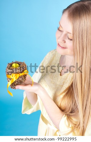 Beautiful young woman holding a nest with Easter egg and yellow tape. Studio shot on a blue background.