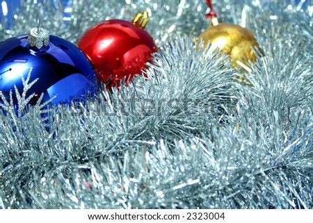 Three celebratory sparkling spheres of dark blue, yellow and red color on a background of a silvery New Year\'s tinsel
