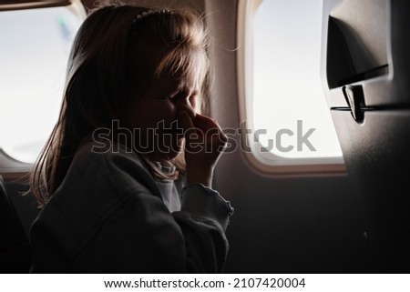 a little girl clamps the nose because of the unpleasant smell in an airplane seat by the window. flights with children in economy class. the smell of sweat, fumes and dirty feet from passengers  Foto stock © 
