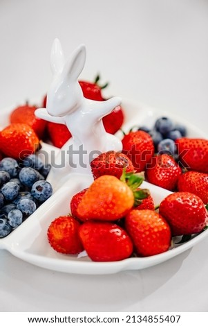 strawberries and blueberries in a white compartmental dish with rabbit. beautiful plate for appetizers, desserts and fruits. berries for the holiday and for every day. 商業照片 © 