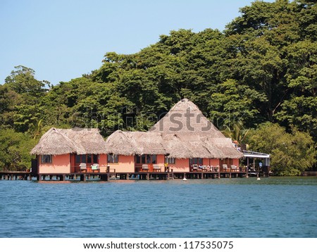 Tropical resort with thatched cabins over the water and lush vegetation in background, Caribbean sea