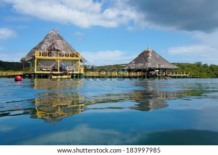 From water surface, tropical bungalow and restaurant on stilts over the sea with palm thatched roof, Colon island, Caribbean, Bocas del Toro, Panama