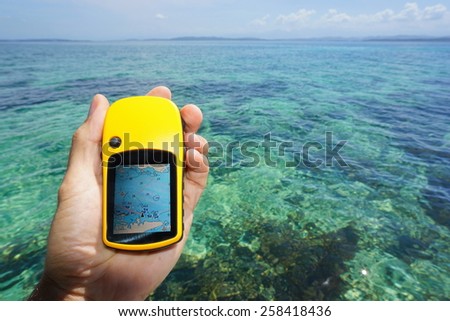 Hand holding a GPS navigator with marine map, over the water of the Caribbean sea