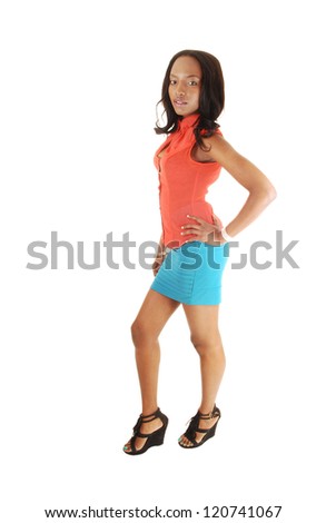 A tall young black woman standing for white background in the studio in an orange blouse and turquoise skirt and high heels.