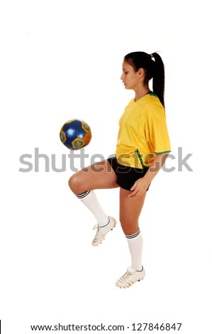 A pretty teenage girl standing in the studio in her soccer uniform and playing with the football, her hair in a ponytail for white background.