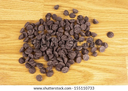 A hand full of brown chocolate chips in a closeup picture lying on light brown wood panels.