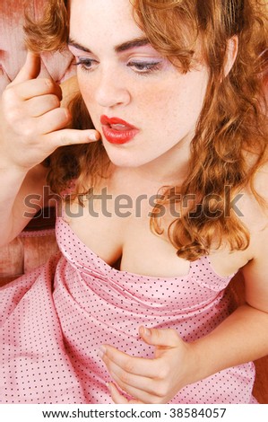 A young red haired woman sitting on a pink sofa in a pink dress fixing her lips, view of the nice breasts.