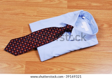 A light blue dress shirt on a wood surface with an red and black tie for sale in the store.
