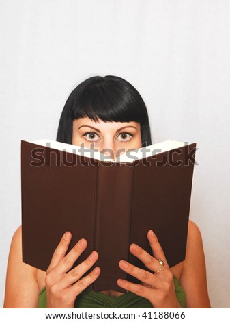 An pretty black haired girl reading in an big book.