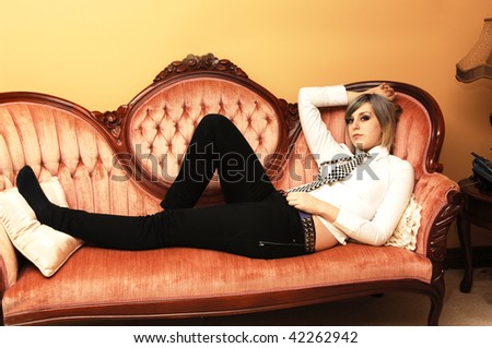An pretty young girl in a blouse and black and white tie lying on a pink sofa looking at the camera.