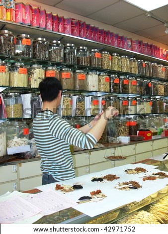 An Chinese herb store with a young man weighing out the amount from an prescription from an Chinese herb doctor.