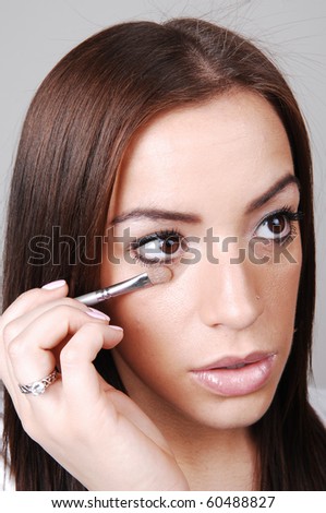A young pretty girl put the last bit of makeup on her face, over light gray background.
