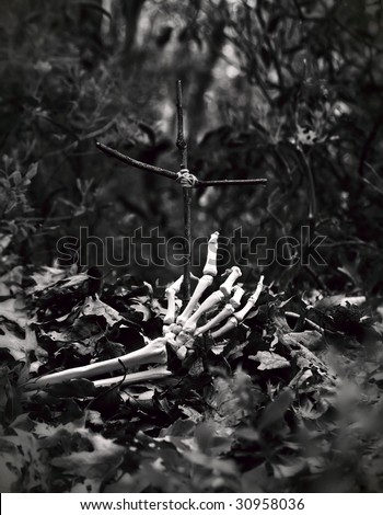skeleton hand coming out of the ground, reaching for a crudely made cross