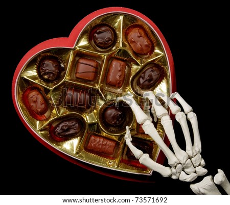 skeleton hand selecting a candy from a valentine\'s box of chocolates, isolated on black