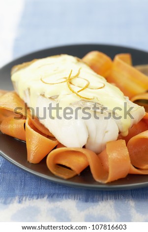Piece of cod with white butter sauce and thin carrot strips