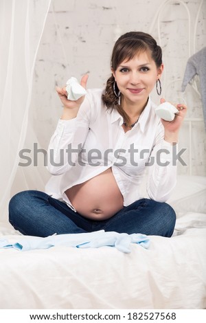 young pregnant woman sit with clothes on white bad in light  home bedroom
