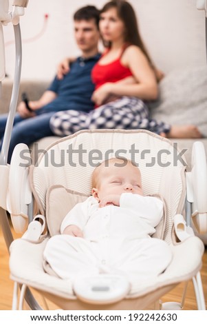 Young parents watchin TV while their baby sleeping in his cradle