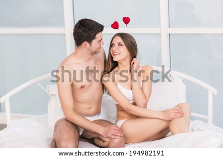 Valentine\'s day couple young lovely together sit in a bed, happy smile looking at camera, concept hearts flying around
