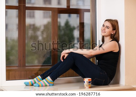Beautiful girl with a Cup of tea sitting on the window sill