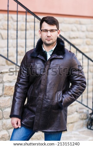 Young man stands with his back against a brick wall while looking in camera