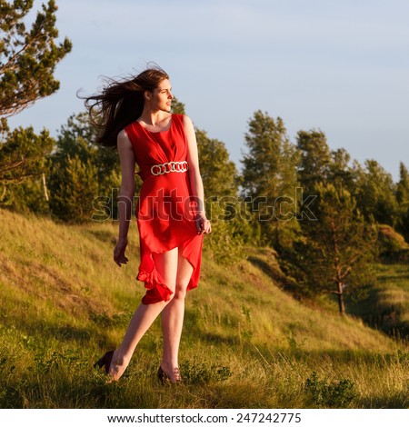 Beautiful girl at precipice. Wind curves her dress and hairs
