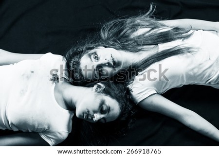 Two young beaten women with cuts and bruises lie down on the floor on black background