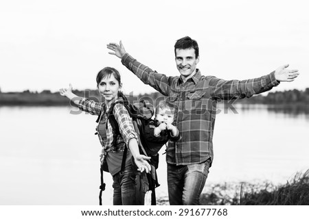 Happy family outdoors with hands outstretched. Baby boy in backpack carrier on walking tour.