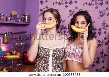Two housewifes in kitchen room imitate smile with bananas
