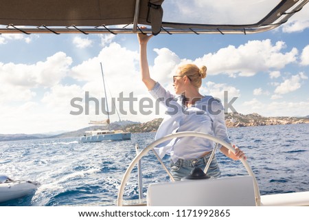 Foto Bild Attraktive blonde Skipperin, die das schicke Katamaran-Segelboot an einem sonnigen Sommertag auf ruhigem blauen Meerwasser steuert.