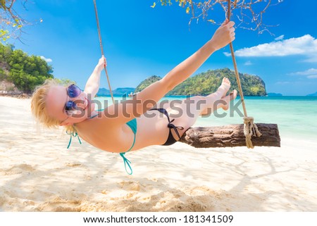 Lady swinging in shade on picture perfect tropical beach with view of island and turquoise coral reef on a sunny summer day.