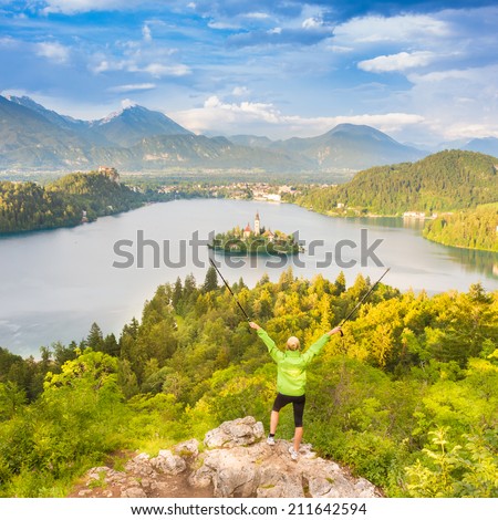 Made it. Young spoty active lady with hiking sticks and hands rised admiring beautiful nature around Bled Lake in Julian Alps, Slovenia.