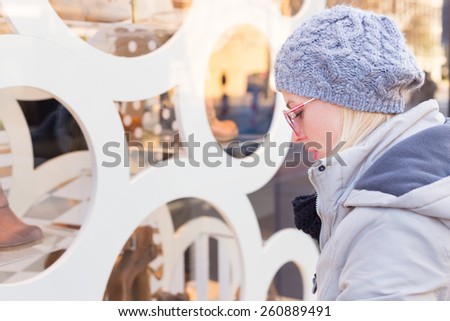 Casualy winter dressed lady window shopping in front of sinfully expensive boutique store dispaly window. Customer woman in shopping street, looking at window, outdoor.
