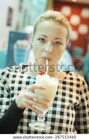 Blond caucasian woman drinking milkshake with straw in american diner.