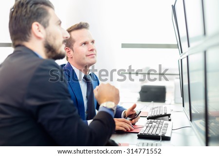 Successful businessmen trading stocks. Stock traders looking at graphs, indexes and numbers on multiple computer screens. Colleagues in traders office. Business success.
