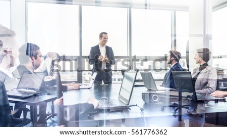 Photo of Successful team leader and business owner leading informal in-house business meeting. Businessman working on laptop in foreground. Business and entrepreneurship concept.