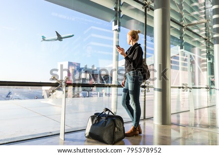 Image, Stock Photo Young casual female traveler at airport, holding smart phone device, looking through the airport gate windows at planes on airport runway.