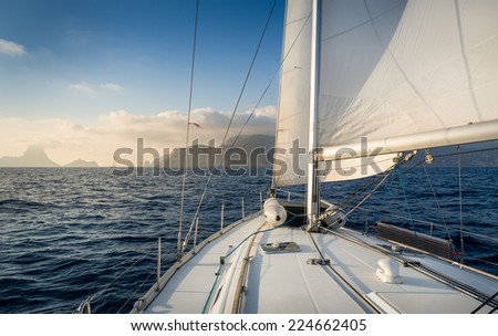 Cruising sailiing yacht with hoisted sails going to rock island. Evening warm light