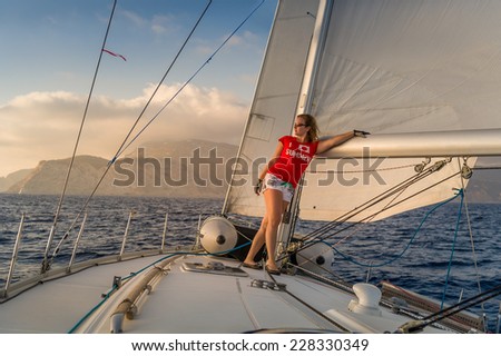 Woman sailor stays at deck of sailing yacht going at full sails to sunset