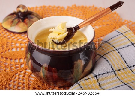 Ceramic butterdish with melted butter, a wooden spoon