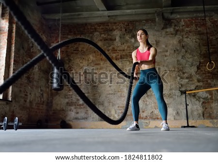 Young woman exercising with battle ropes at the gym. Strong female athlete doing crossfit workout with battle rope. Regular sports boosts immune system and promote good health. Healthy lifestyle
